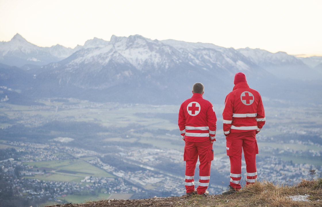 two red cross workers standing on a mountain overlooking a community