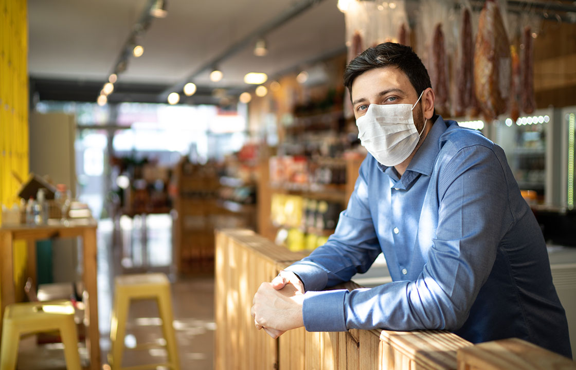 man with mask leaning on a counter in a small business