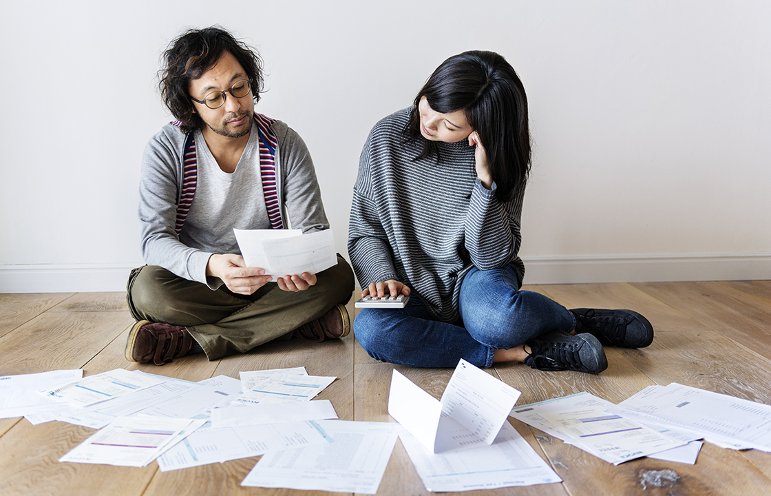 man and woman sitting in front of stacks of bills and crunching numbers on a calculator