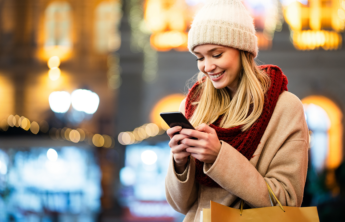 decorative image of a woman looking at her phone with twinkling lights behind her